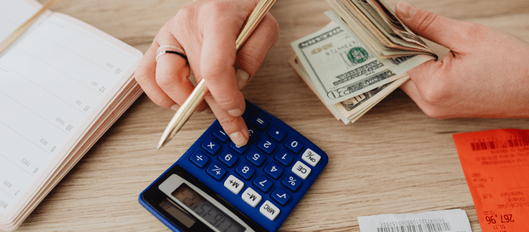 Image of a woman using a calculator at a desk for a post answering the question "how much do secret shoppers make?"
