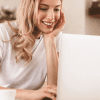 Image of a young woman working on a laptop in her kitchen for a blog post covering how to find mystery shop jobs.