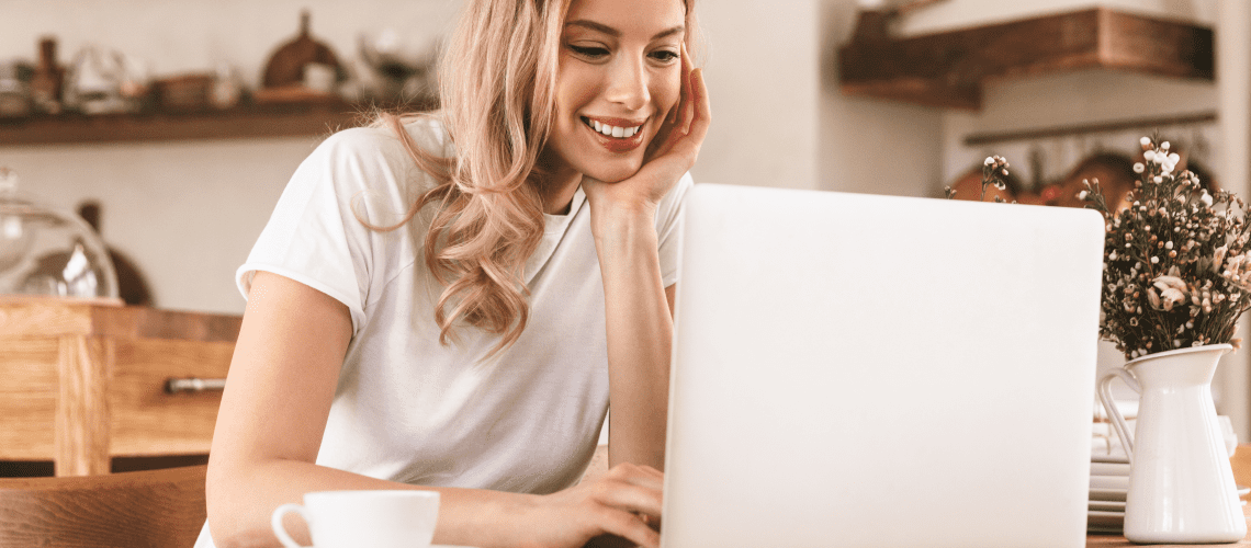 Image of a young woman working on a laptop in her kitchen for a blog post covering how to find mystery shop jobs.