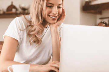 Image of a young woman working on a laptop in her kitchen for a blog post covering how to find mystery shop jobs.