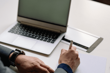 Image of a man at a desk working on his laptop and taking notes for a blog post covering mystery shopping preparation.