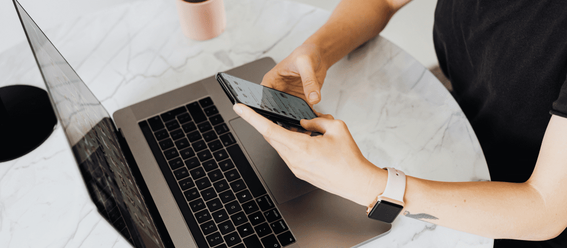 Image of a woman working on her laptop and phone for an article about working with mystery shopping schedulers.